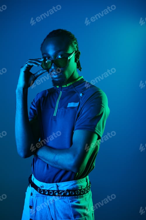 Preview: Stylish African American man confidently poses in a neon-lit studio, showcasing fashion