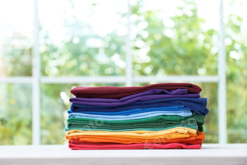 Preview: Stack of bright folded clothes on table against blurred background. Space for text