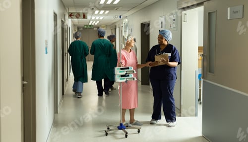 Preview: Diverse female doctor and caucasian senior female patient with iv pole talking in hospital