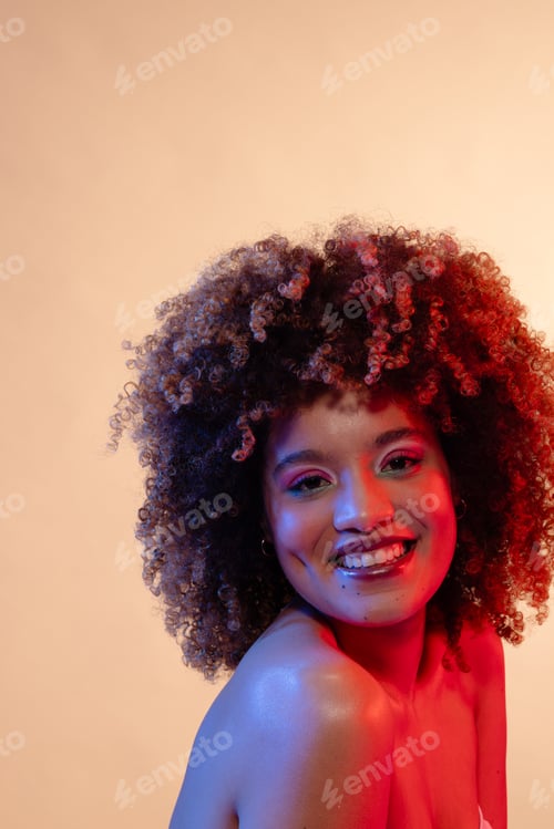 Preview: Smiling biracial woman wearing pink eyeshadow and lipstick in red and blue light, copy space