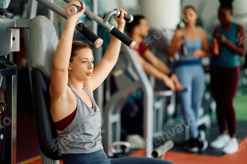 Preview: Young athletic woman doing chest exercises on machine while working out in gym.