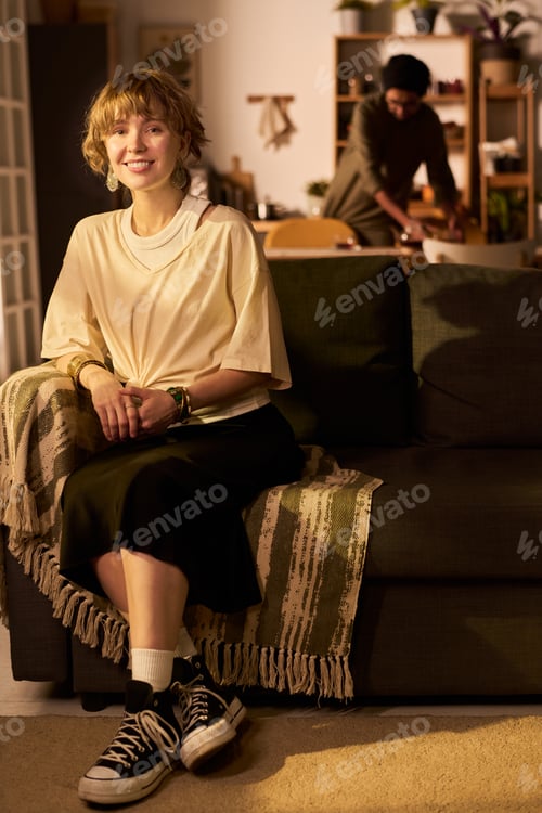 Preview: Portrait of Smiling Woman Sitting on Couch with Friend Cooking