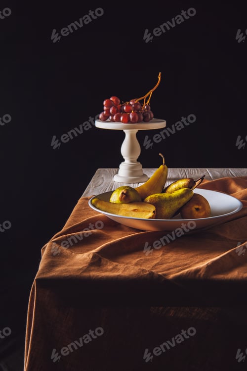 Preview: plate of pears and stand with grapes on table on black
