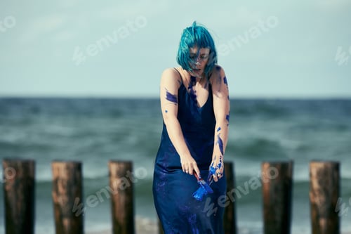 Preview: Artistic blue-haired woman performance artist in dress smeared with blue gouache paints on her body
