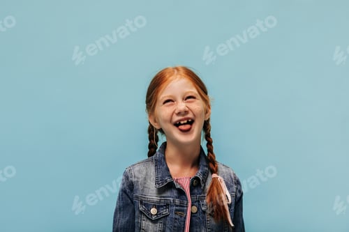 Preview: Happy little girl with ginger hair and lovely freckles in stylish denim jacket and red dress showin