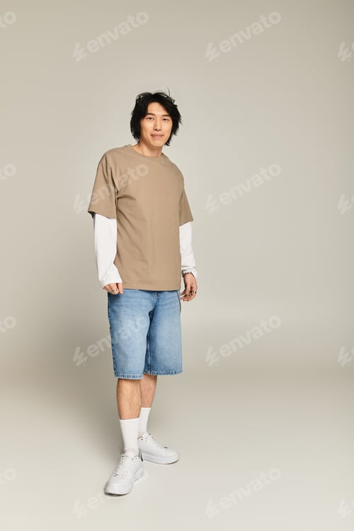 Preview: Stylish young asian man poses confidently in casual urban attire against a minimalistic backdrop