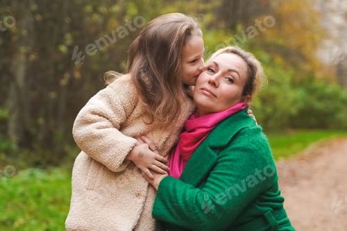 Preview: Cuddling mother with daughter in park. Smiling family portrait shows love, affection, support