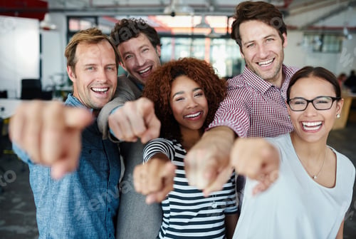 Preview: Portrait of a group of smiling coworkers pointing at the camera while standing in an office