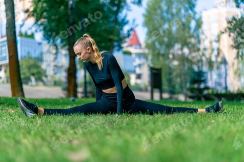 Preview: A young beautiful girl sits on splits and does stretching after training in morning in the park