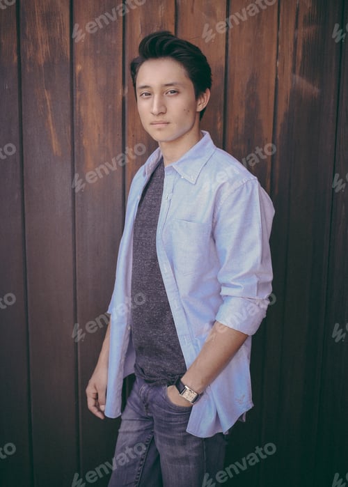 Preview: Portrait of a young man standing in front of a rustic wood building with his hand in his pocket