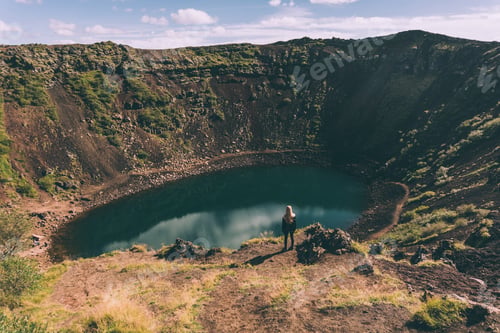 Preview: back view of young woman looking at beautiful crater lake in Iceland