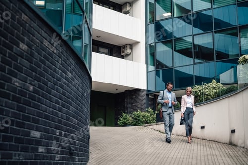 Preview: Business colleagues walking past modern corporate building