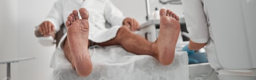 Preview: Smiling client sits in armchiar while woman prepares equipment in salon, focus on bare feet
