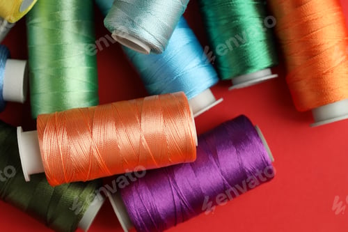 Preview: Different spools of sewing threads on red background, top view