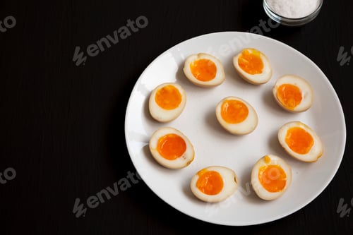Preview: Homemade Unami Soy Sauce Eggs on a white plate on a black background, side view. Copy space.