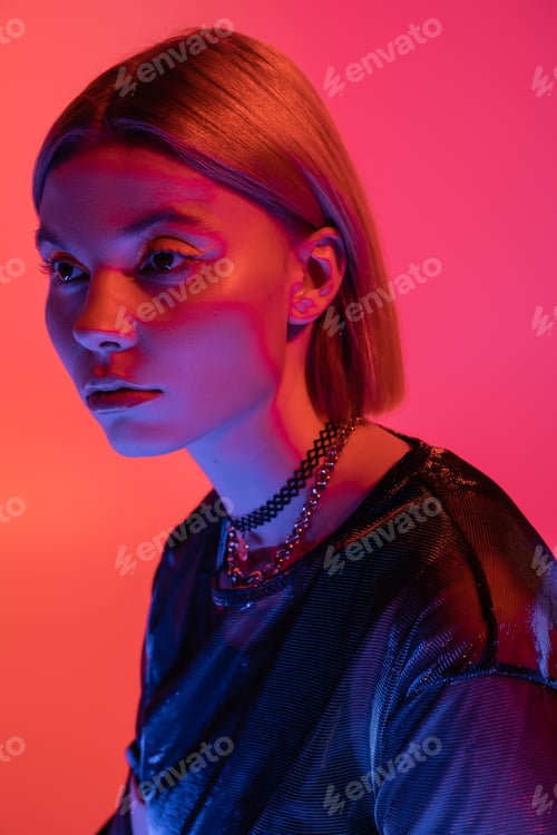 Preview: portrait of trendy woman in necklaces posing in neon light on coral and pink background