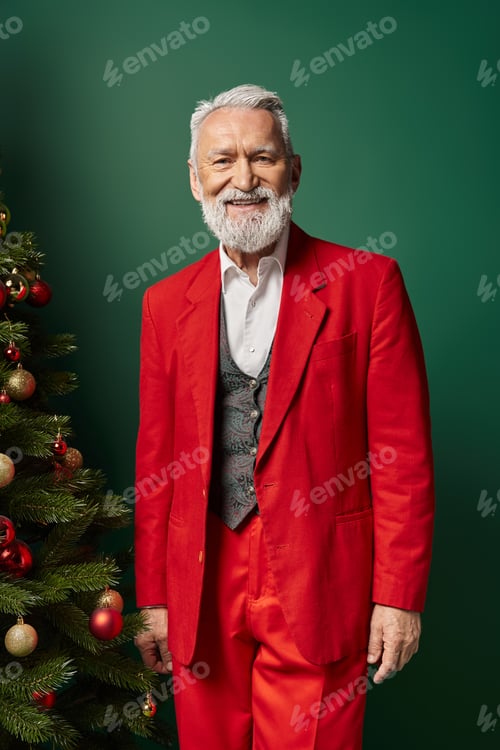 Preview: cheerful man in stylish Santa red costume posing near fir tree with baubles, Christmas concept