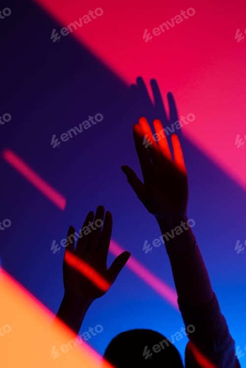 Preview: Woman arm gesturing with open hand over fashion blue, orange and pink wall, neon red light on wrist