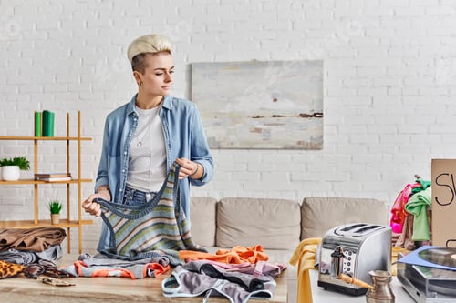 Preview: sharing economy, tattooed and stylish woman with knitted tank-top near table with second-h