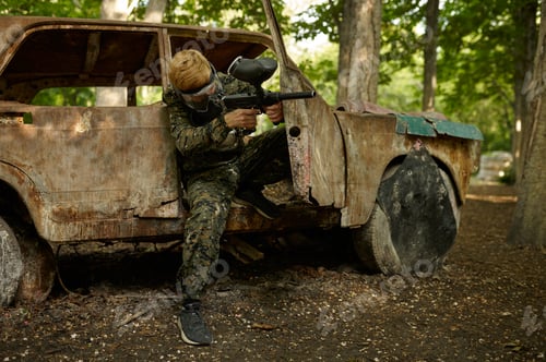 Preview: Paintball player in uniform and mask in forest