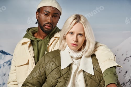 Preview: portrait of voguish multiracial couple in warm vibrant attire looking at camera, winter concept