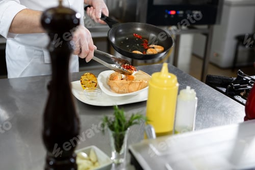 Preview: Beautiful man chef preparing dish with shrimps at table in kitchen