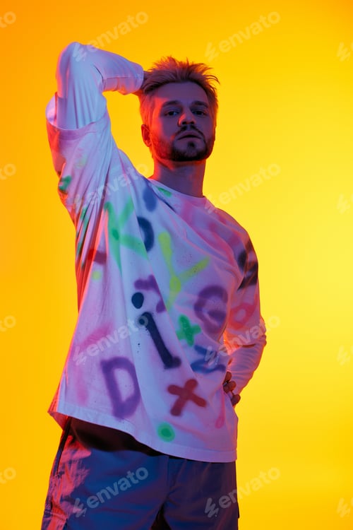 Preview: Young man posing confidently against a vibrant yellow backdrop in artistic attire