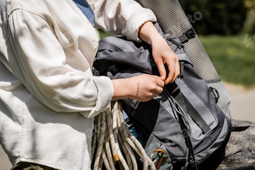 Preview: Cropped view of young tattooed female hiker in casual clothes checking backpack with equipment and