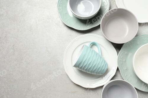 Preview: Beautiful ceramic dishware and cup on light grey table, flat lay. Space for text
