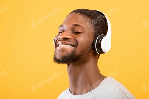 Preview: Favorite song. Carefree african american guy in headphones listening music with closed eyes, yellow