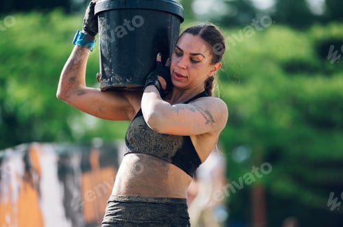 Preview: Female participating in an OCR race while carrying heavy barrel on her shoulder