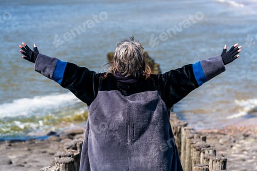 Preview: Mature woman with arms spread by the sea