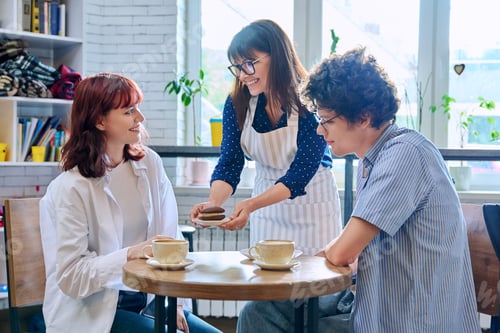 Preview: Woman in an apron with cup of coffee and plate of cake serving young people in cafeteria