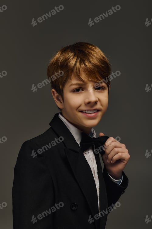 Preview: Elegant preteen boy in a stylish tuxedo with bow tie posing in a studio setting