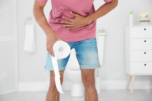 Preview: Young man with bath tissue standing near toilet bowl at home