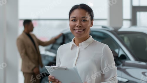 Preview: Portrait of smiling African American woman car saleswoman dealer consultant posing in dealership