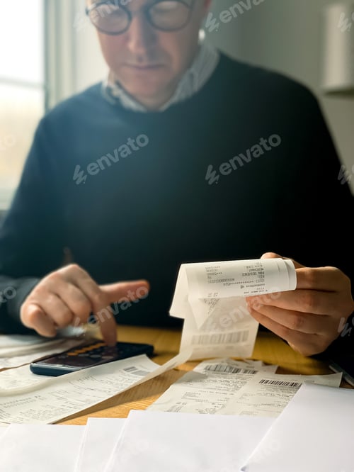 Preview: Man is making audit of household expenses using calculator and notebook. Lots of receipts and bills