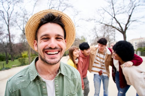 Preview: Young smiling guy looking at the camera outdoors with group of friends. Happy people having fun