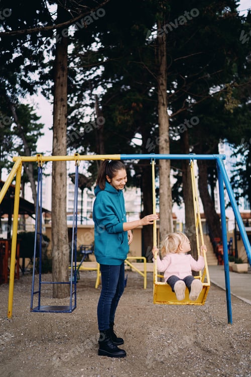 Preview: Mom swings a little girl on a swing in the park and looks at her