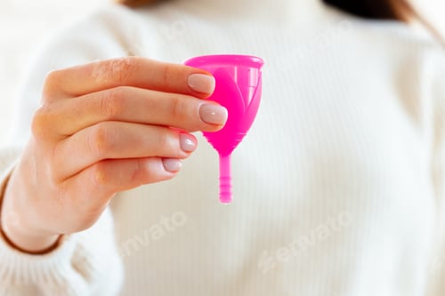 Preview: Woman in white sweater holding pink menstrual cup in hands close up