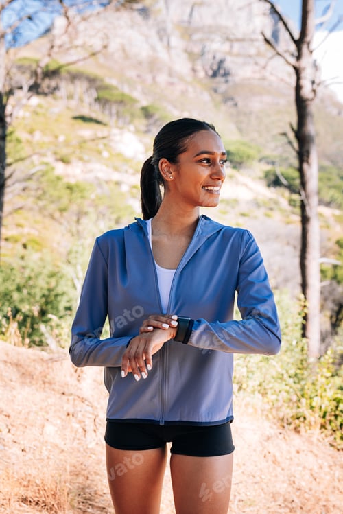 Preview: Side view of cheerful woman athlete looking away. Smiling female checking smartwatch outdoors.