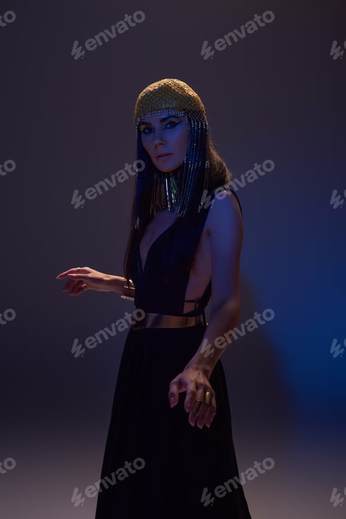 Preview: Brunette woman in traditional Egyptian look looking at camera on brown background with blue light