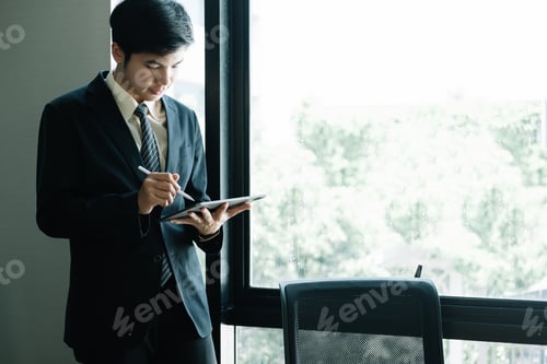 Preview: Young Asian Businessman Standing and using tablet at office