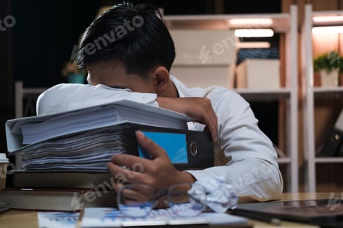 Preview: Young tired businessman lying on table at night office.