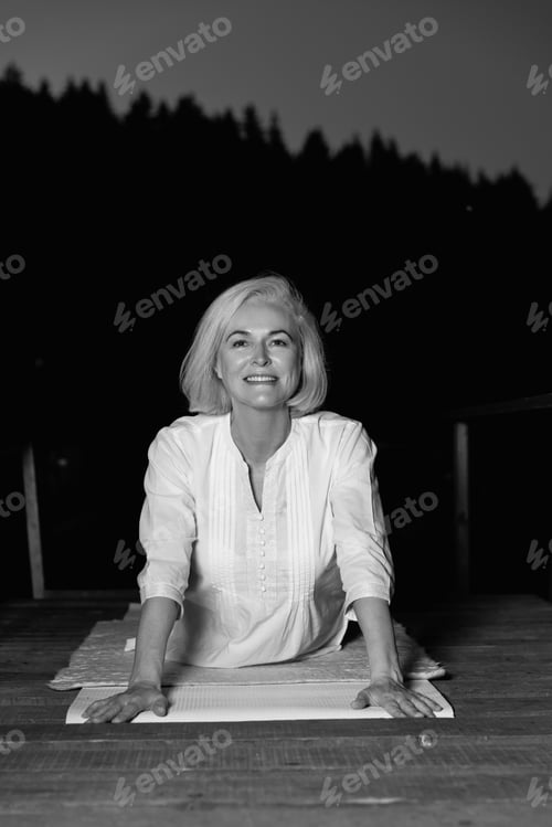 Preview: middle aged woman doing yoga outdoors in forest