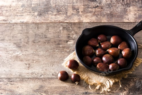 Preview: Chestnuts roasting in a cast iron pan on rustic wooden table