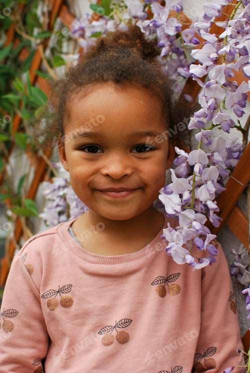 Preview: Portrait of a toddler girl in front of purple wisteria flowers - petals pink mixed race diversity
