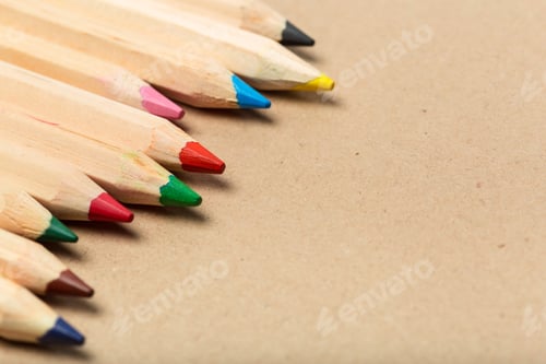 Preview: Colored pencils are arranged in a line on brown paper surface