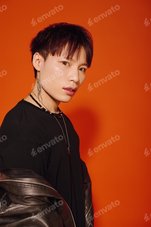 Preview: Stylish young Asian man poses against vibrant orange background with confident expression