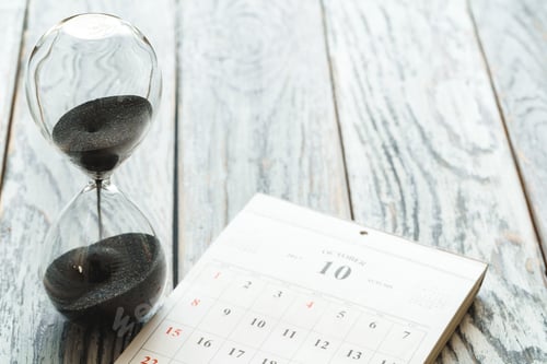 Preview: Hourglass with calendar on wooden desk close up